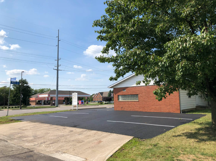 Suburban parking lot beside a red brick building and tree under a blue sky