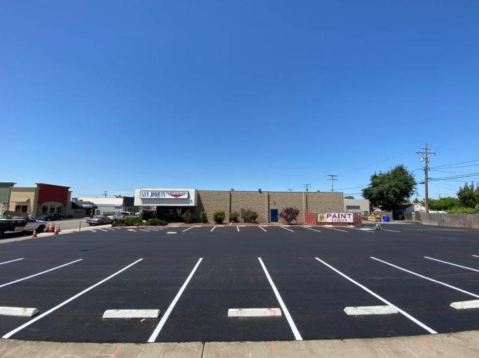 Empty parking lot in front of a low commercial building under a clear blue sky.