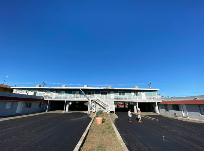 Motel-style building with outdoor stairs, a clear blue sky, and two people near the entrance.
