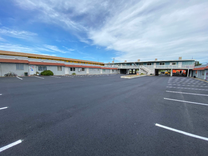 Empty parking lot beside low industrial buildings under a cloudy sky