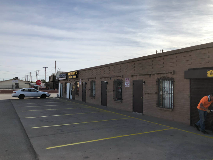 Strip mall parking lot with a white car, storefronts, and a person in orange near the right side.