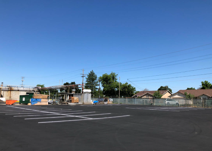 Empty parking lot beside low buildings under a clear blue sky