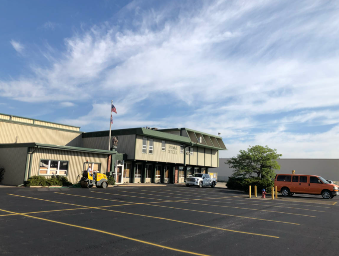 Large building with an American flag and empty parking lot under a blue, cloudy sky
