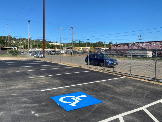 Accessible parking space marked in blue paint in a mostly empty lot near a chain-link fence.