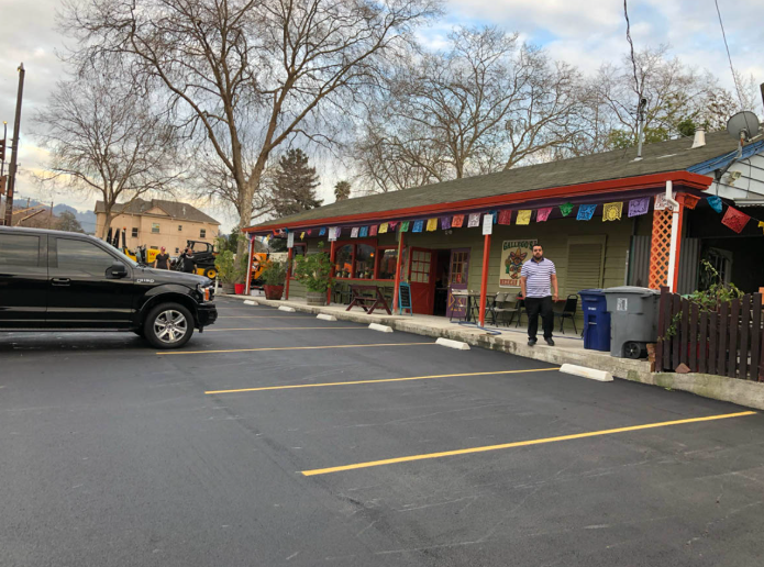 Parking lot beside a colorful storefront, with a black SUV and a person standing near the entrance.