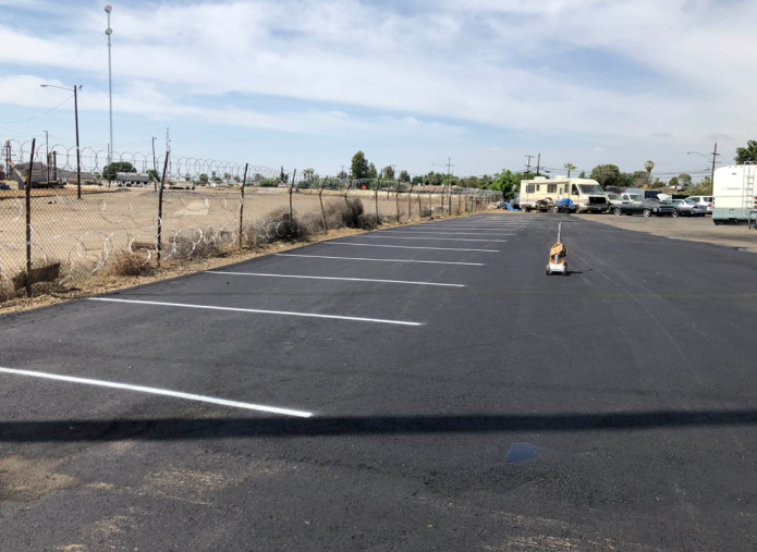 Empty parking lot with fresh asphalt, white space lines, and a single cone under a clear sky