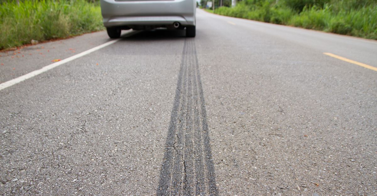 Rear view of a car driving on a road with a dark skid mark down the center