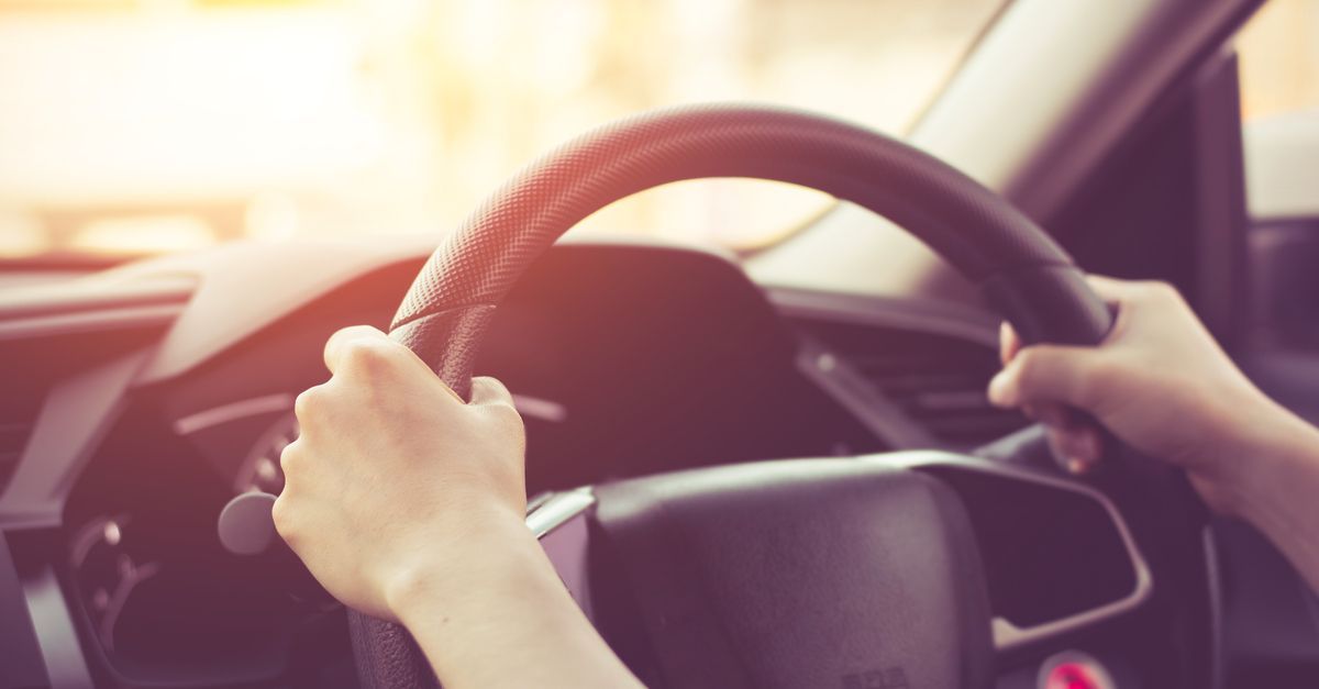Hands gripping a steering wheel inside a car, with warm sunlight streaming through the windshield.