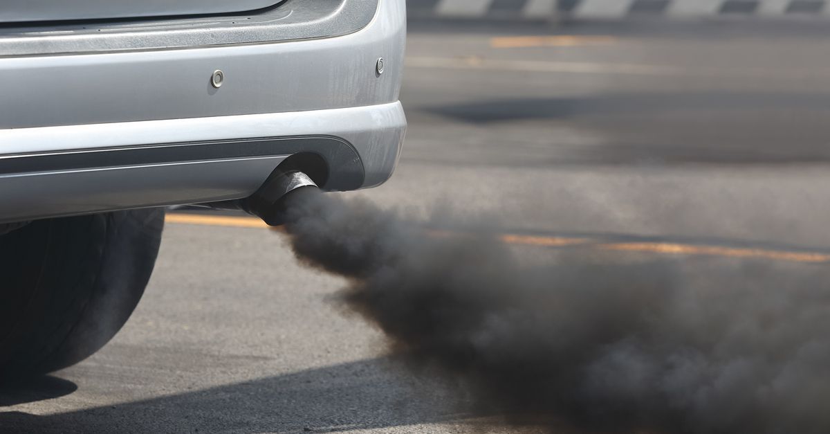 Rear of a silver car with a black exhaust plume billowing onto the road