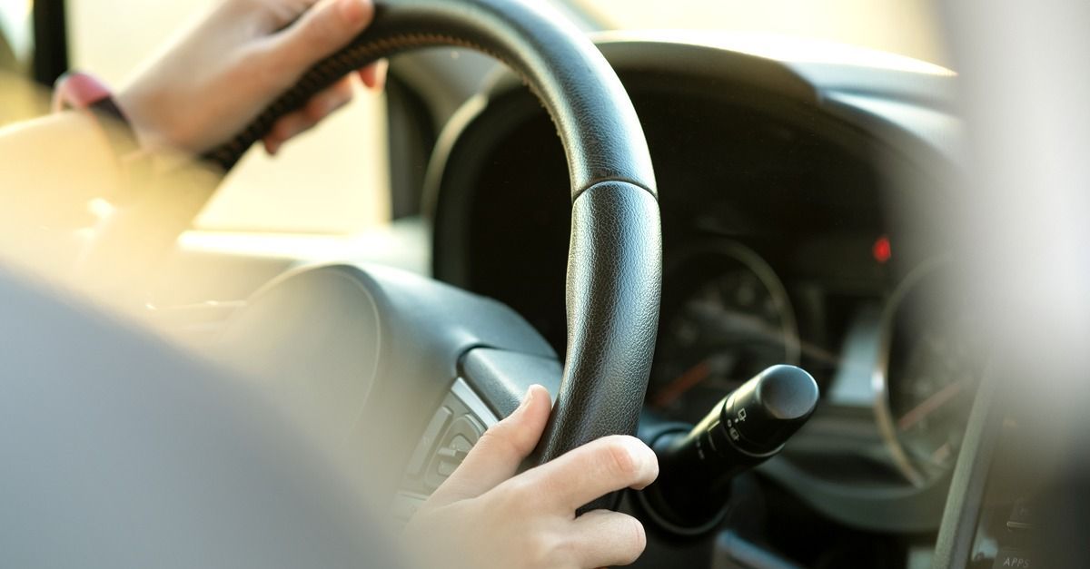 Hands on a steering wheel inside a car, with the dashboard visible.