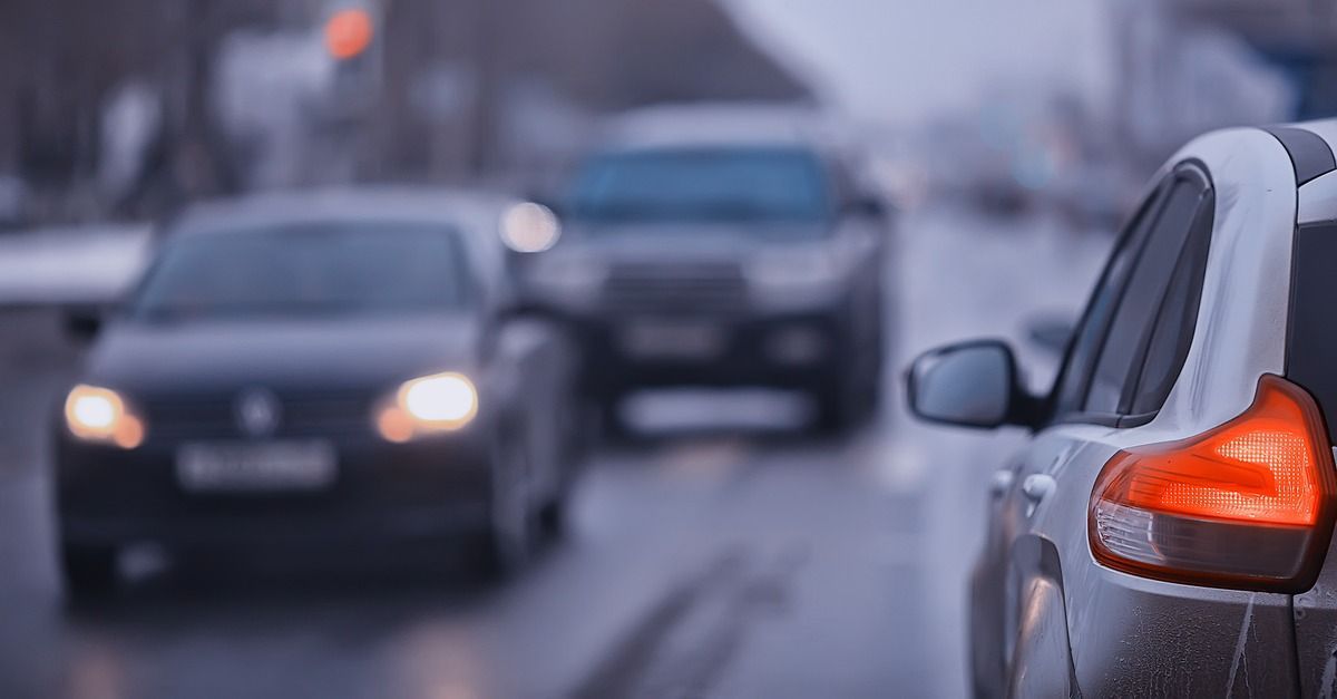 Cars driving in rainy traffic, with a silver car’s red taillight in the foreground.