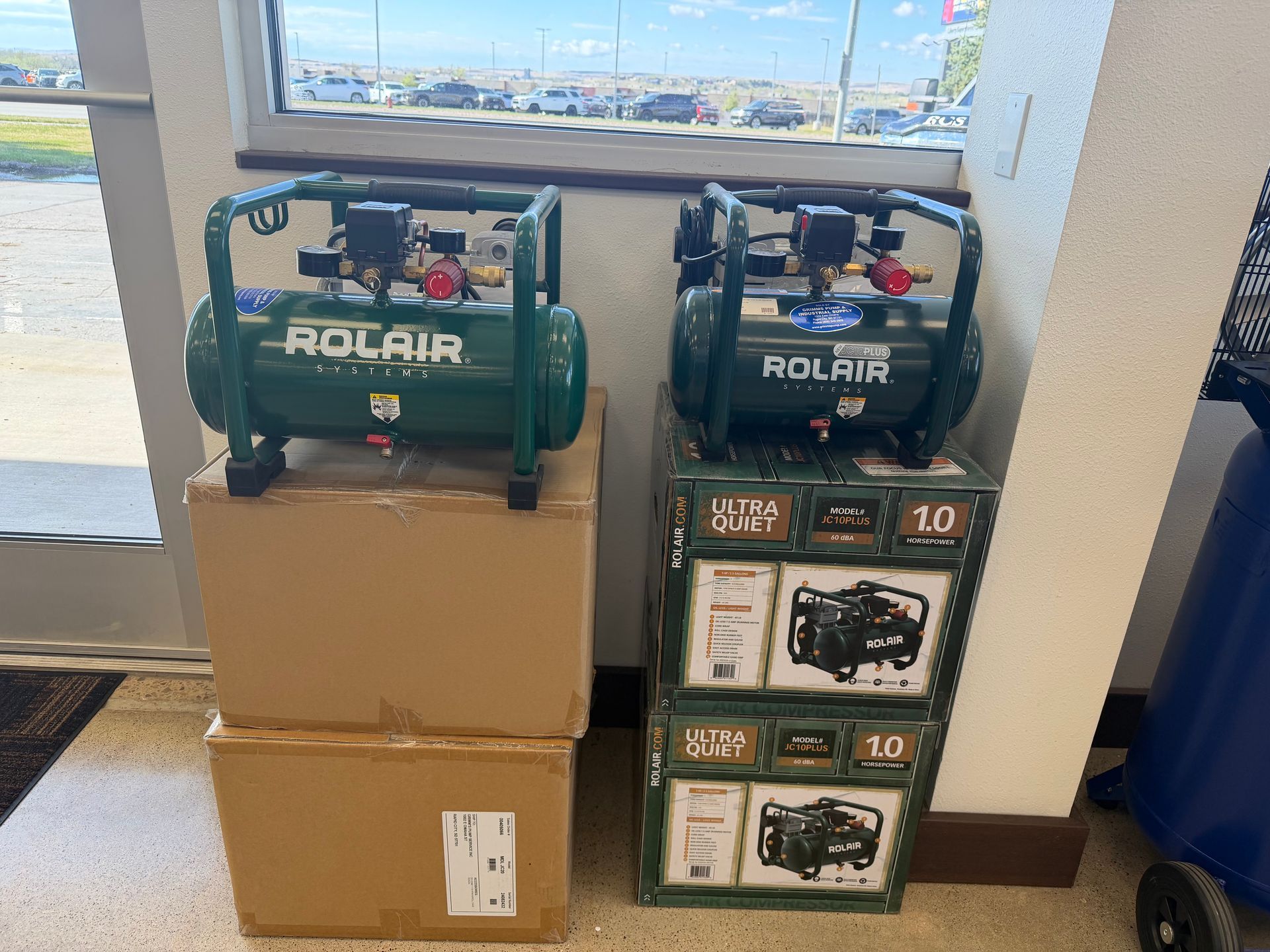 Two green Rolair air compressors displayed on cardboard boxes in a store window.