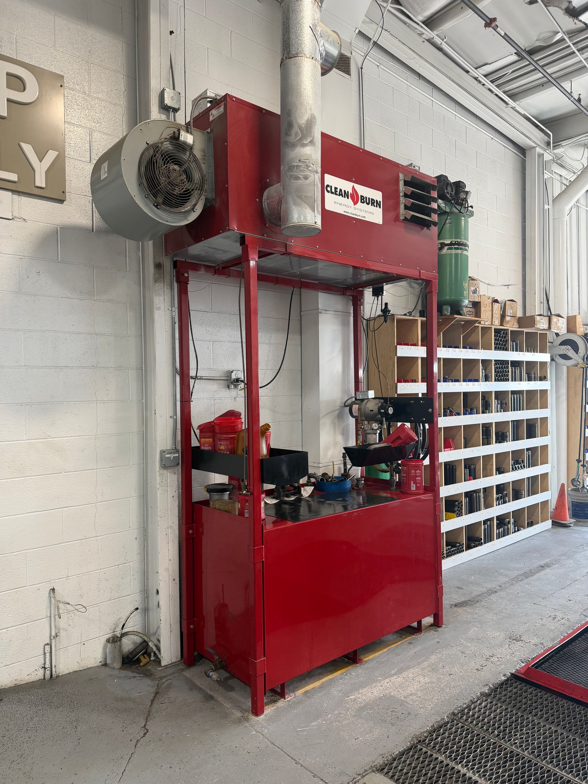 Red industrial machine by a wall in a workshop or garage, with tools and shelving nearby.