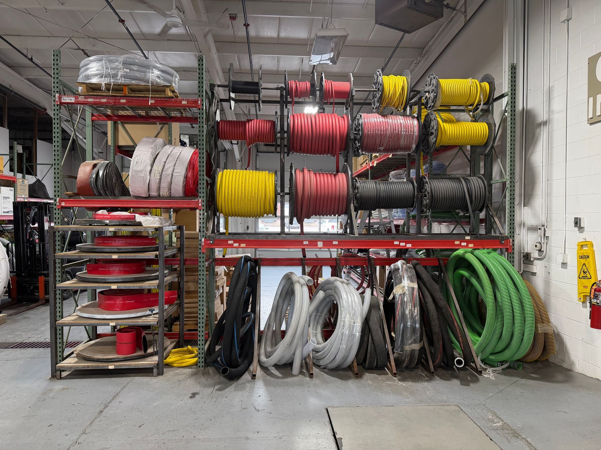 Industrial warehouse rack with coiled hoses and cables in red, yellow, black, and green on metal shelves
