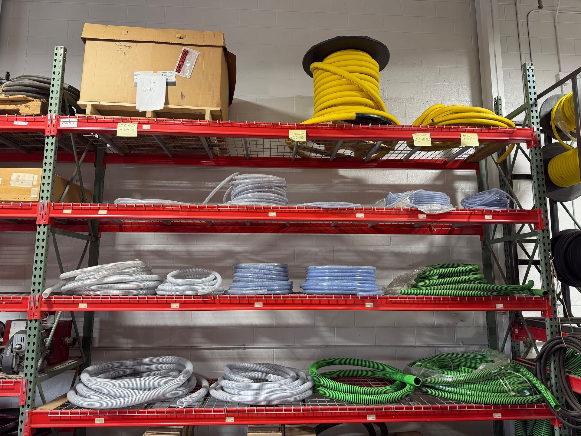 Shelved coils of gray, blue, and green cable in a warehouse storage rack with boxes on top