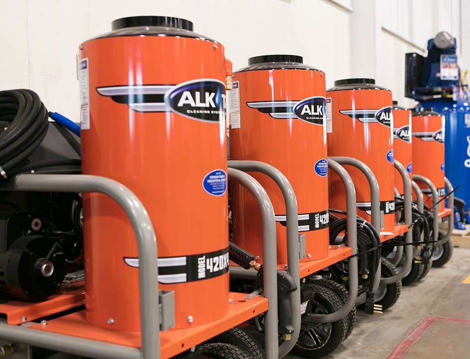 Row of orange industrial vacuum machines with black hoses in a workshop