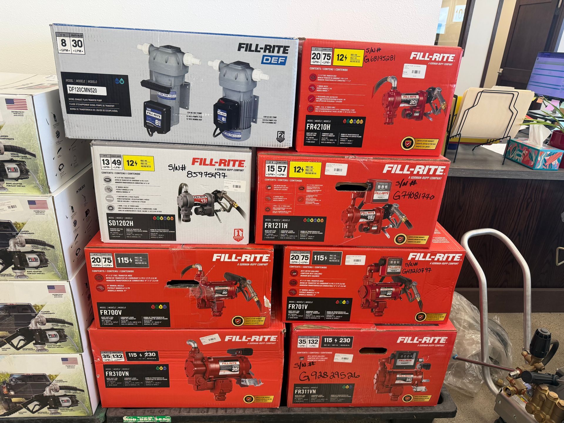 Stack of red and gray product boxes with tools on a countertop in a store or workshop.