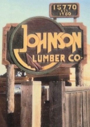 A wooden sign for Johnson Lumber Co. with the address 15770 and the established year 1960, set against a wooden fence.
