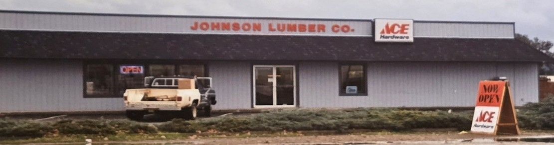 A single-story Johnson Lumber Co. store with an Ace Hardware sign, a parked pickup truck, and a sidewalk sign in front.
