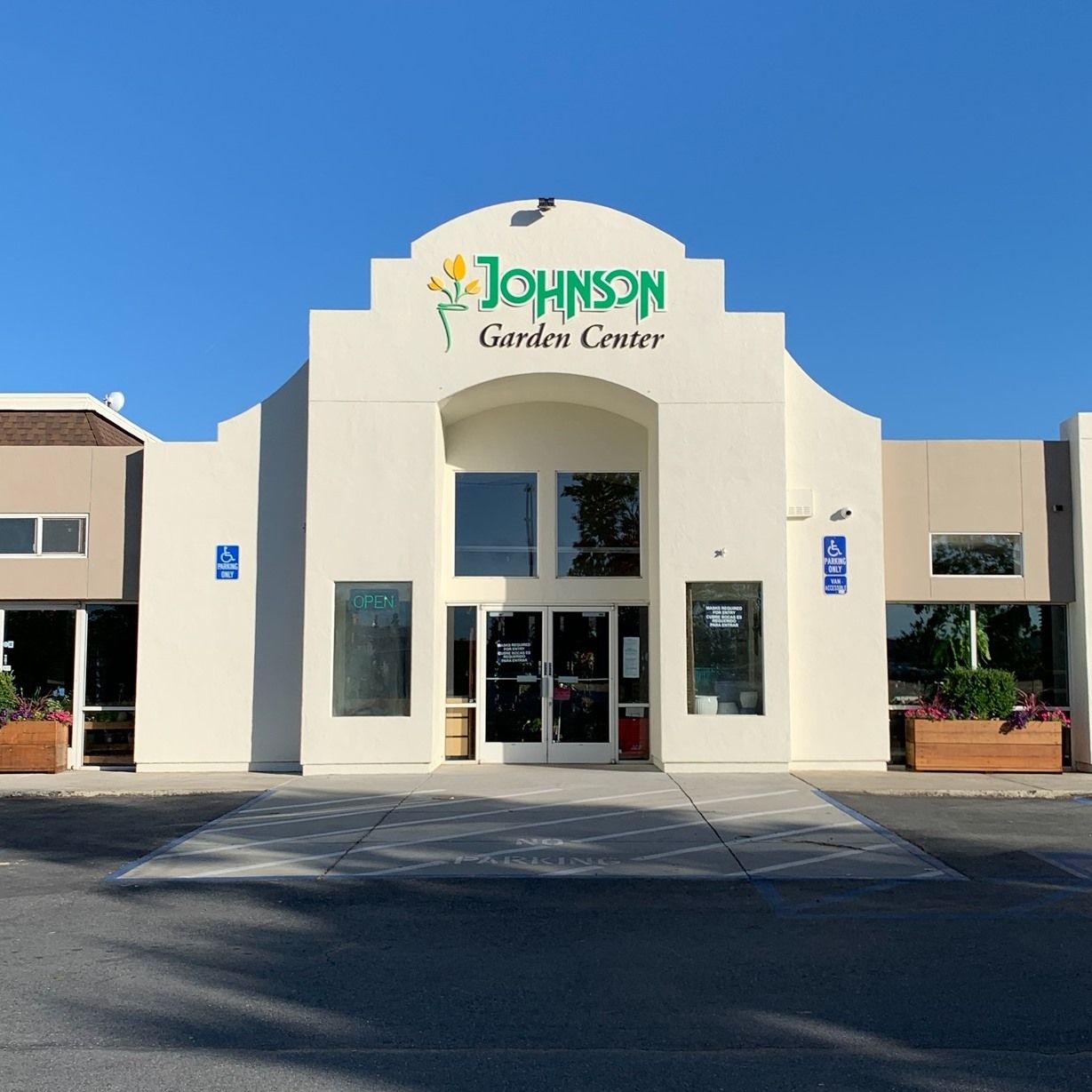 Johnson Garden Center, a beige building with a white arched facade, glass doors, and a parking lot under a blue sky.