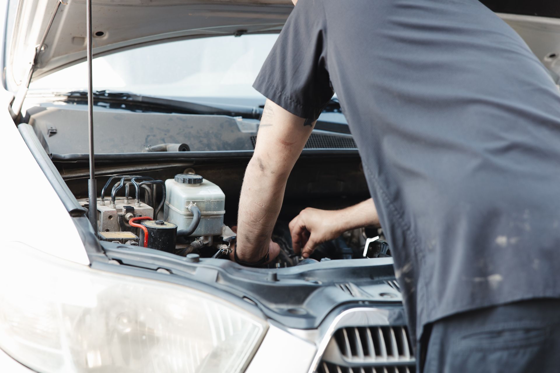 A mechanic is working under a lifted vehicle in a garage, tightening parts near the rear axle.
