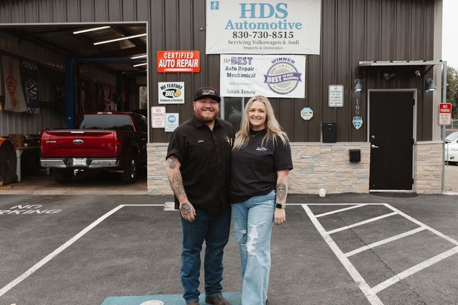 Two people are standing outside the HDS Automotive garage with a red pickup inside.