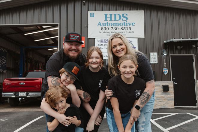 Family posing outside HDS Automotive shop, smiling in front of a red truck and open garage