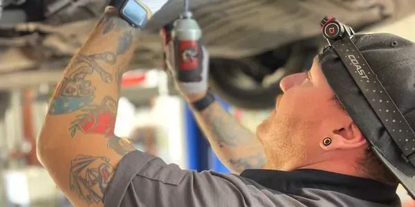 A man is working on a car underneath it in a garage.