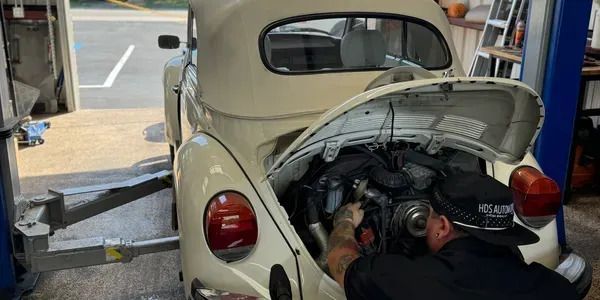 A man is working on the engine of a white car.
