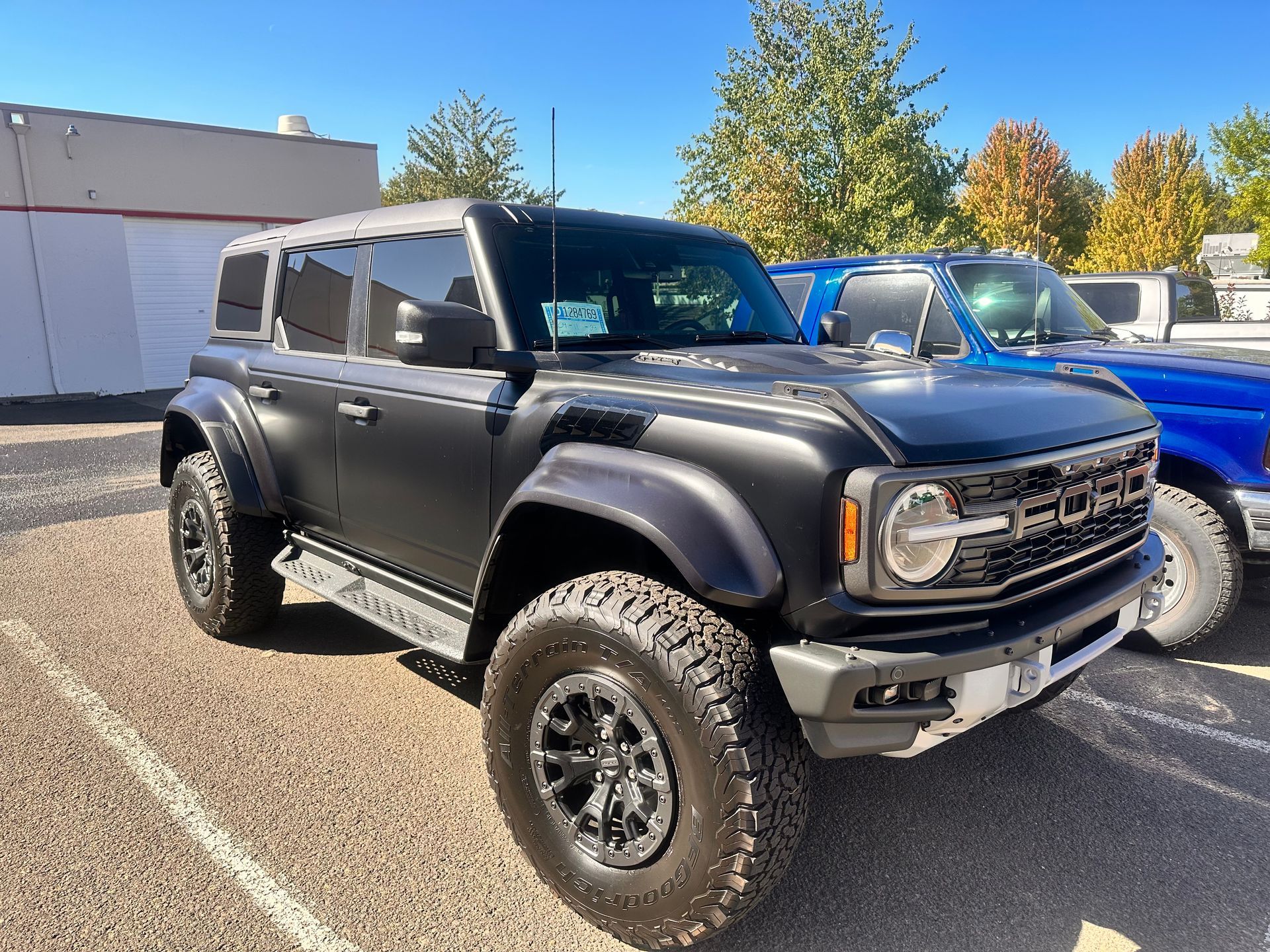 A black ford bronco is parked in a parking lot next to a blue truck.