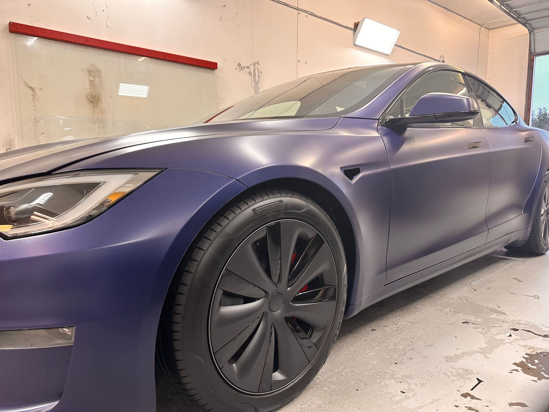 A purple tesla model s is parked in a garage.
