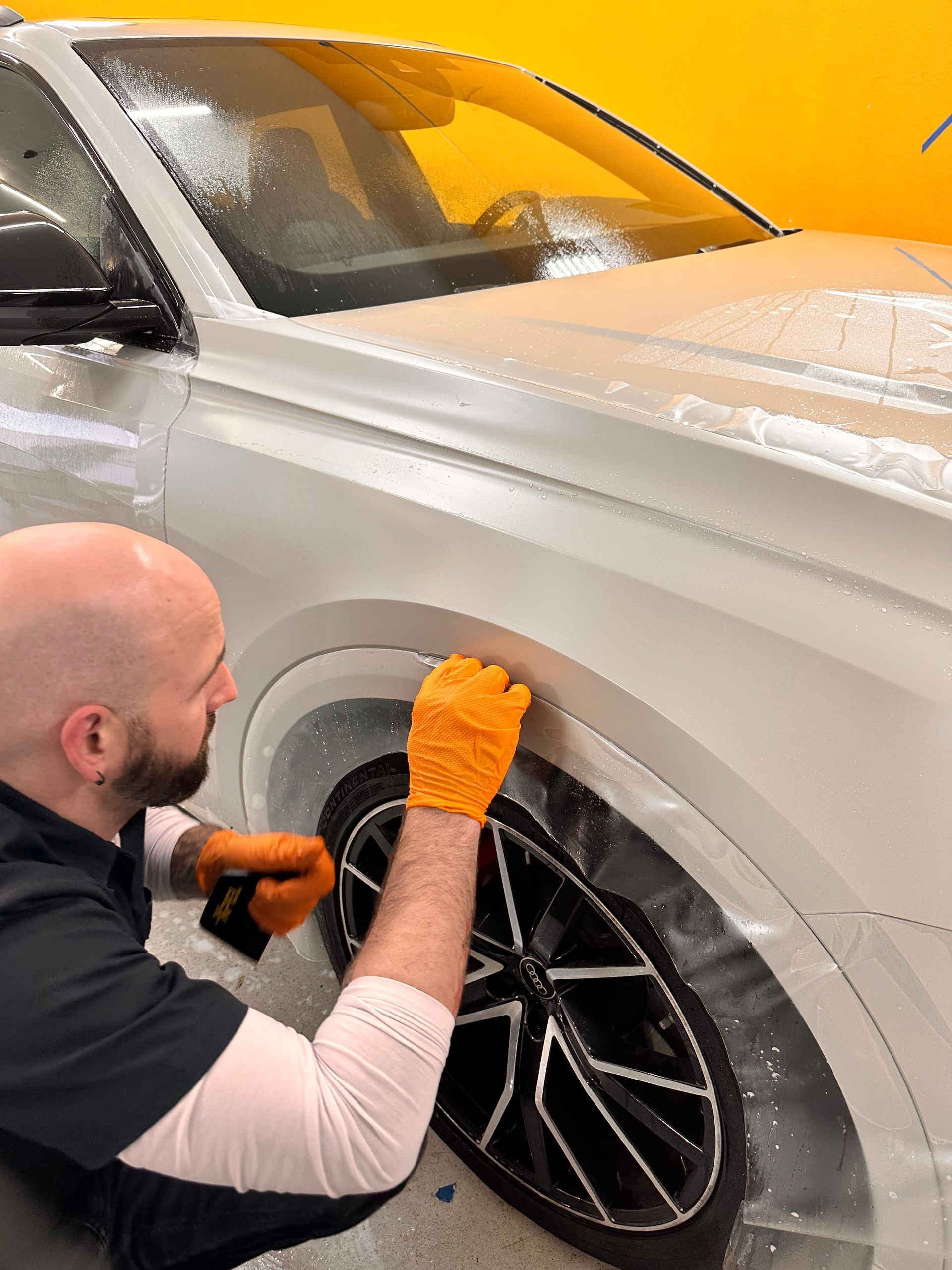 A man is wrapping a white car with plastic wrap.