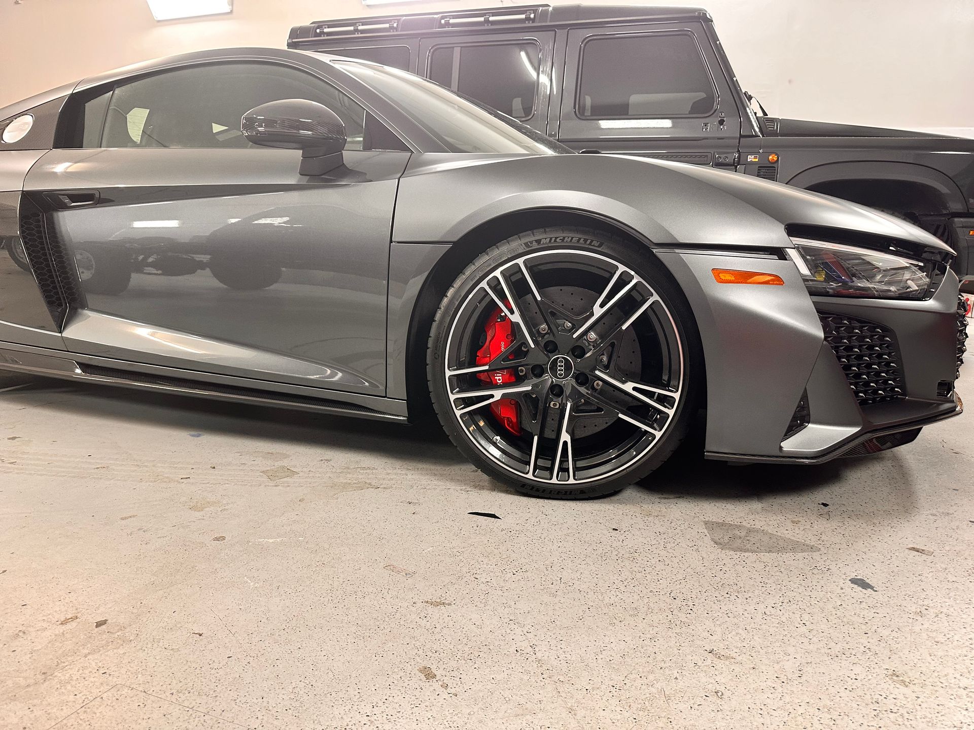A gray audi r8 is parked in a garage next to a black jeep.