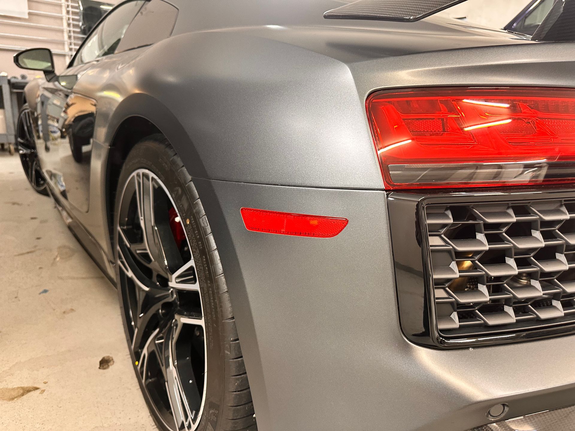 A gray sports car with a red tail light is parked in a garage.