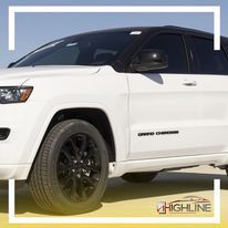A white jeep grand cherokee with black wheels is parked on the beach.