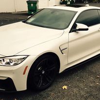 A white bmw m4 is parked in a parking lot next to a green trash can.
