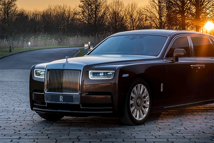 A rolls royce phantom is parked on a brick driveway at sunset.