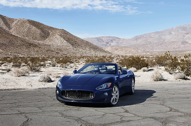 A blue convertible car is parked on the side of the road in the desert.