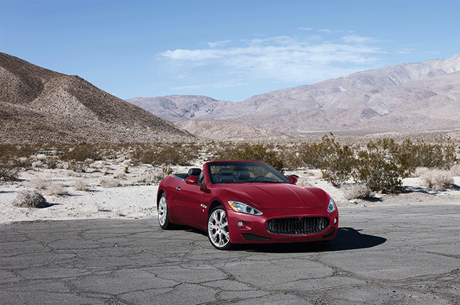 A red sports car is parked on the side of the road in the desert.