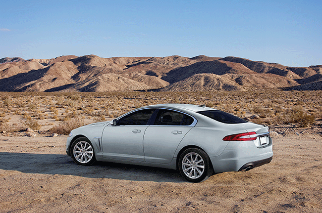 A white car is parked in the middle of a desert with mountains in the background.