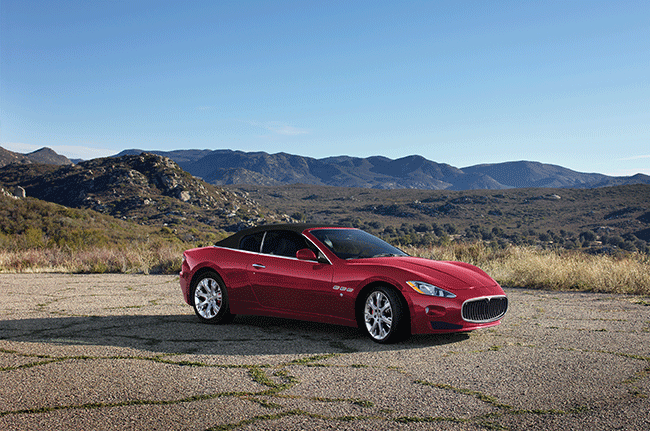 A red sports car is parked on the side of a road in front of mountains.