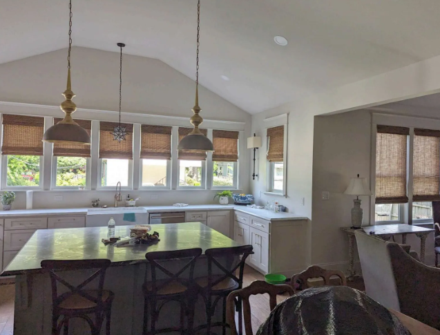 Bright kitchen with a large island, pendant lights, windows, and a dining nook beside a living area.