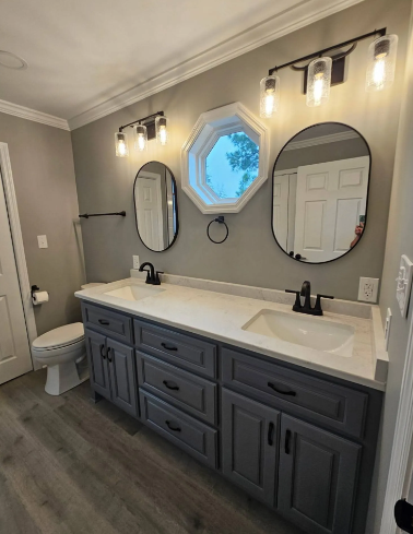 Modern bathroom vanity with double sinks, black fixtures, round mirrors, and wall sconces over gray cabinets.