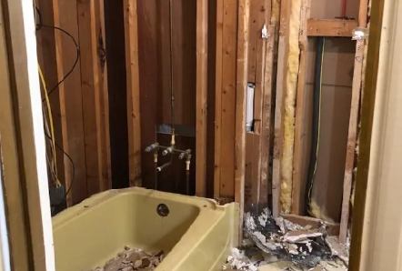 Yellow bathtub in a gutted bathroom with exposed wall studs and construction debris.