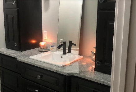 Bathroom vanity with black cabinets, granite countertop, white sink, black faucet, and lit candle beside a mirror.