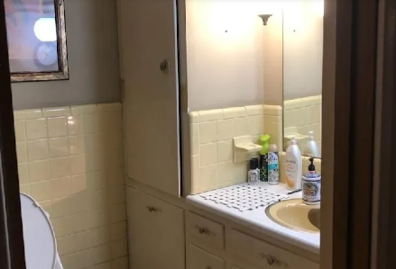 Small bathroom vanity with sink, mirror, toiletries, and white tile walls