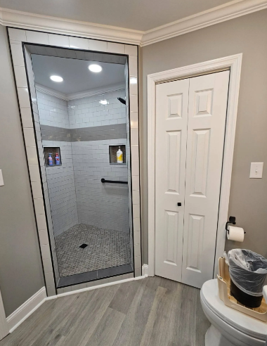 Bathroom with glass shower stall, white door, and gray tile walls and floor