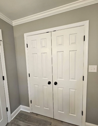 White double closet doors with black knobs in a gray room with crown molding and wood flooring