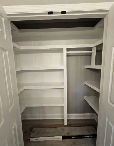 Empty walk-in closet with white shelves, hanging rods, and gray walls.