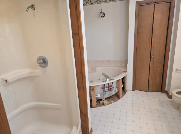 Bathroom under renovation with unfinished tub alcove, shower stall, and wood-framed mirror cabinet.